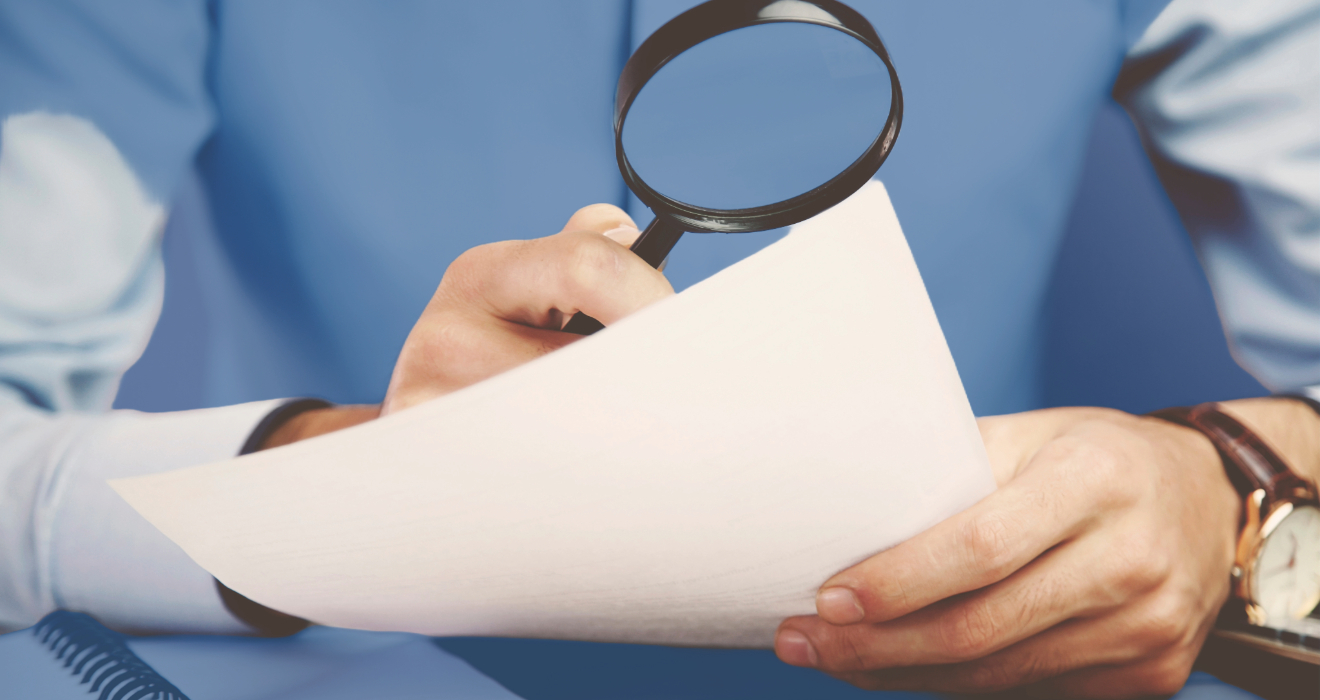 person holding magnifying glass and paper